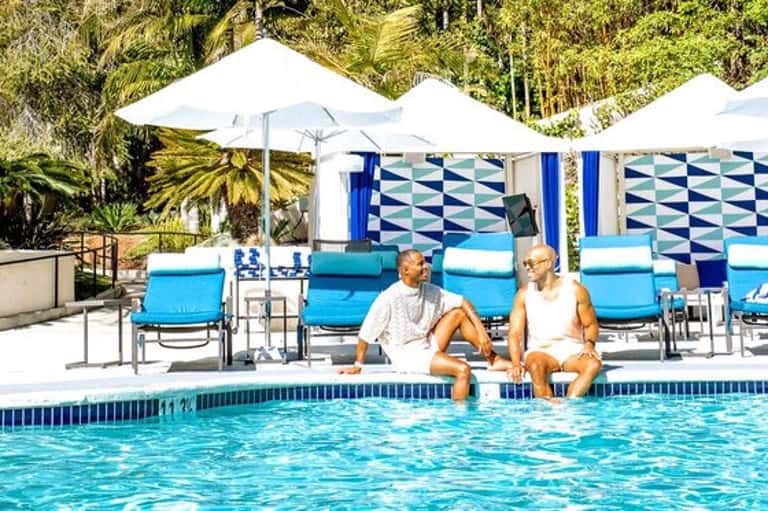 Couple relaxing in resort pool with blue loungers and white umbrellas under palm trees