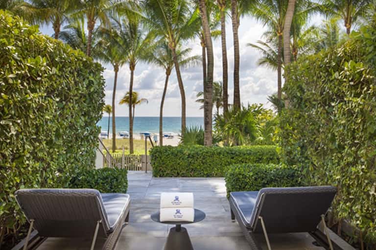 Palm-lined tropical beach pathway with lounge chairs, ocean view, and lush vegetation