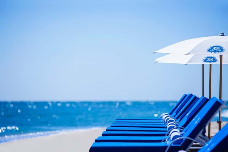Row of blue beach loungers with white umbrellas along sandy shore facing ocean