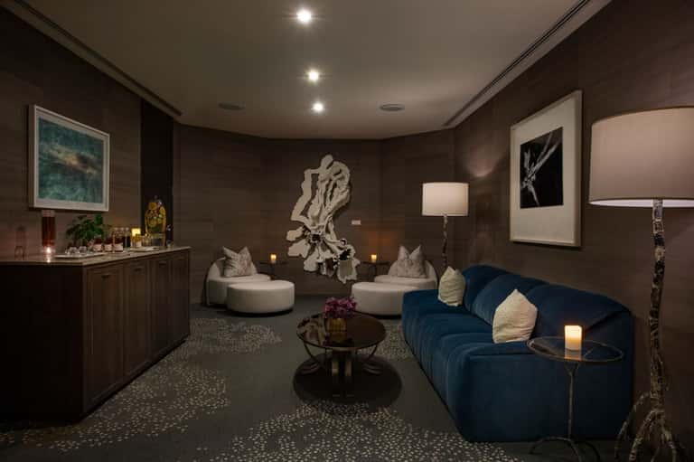 Luxury spa lounge with dark wood walls, blue curved sofa, and artistic sculptures