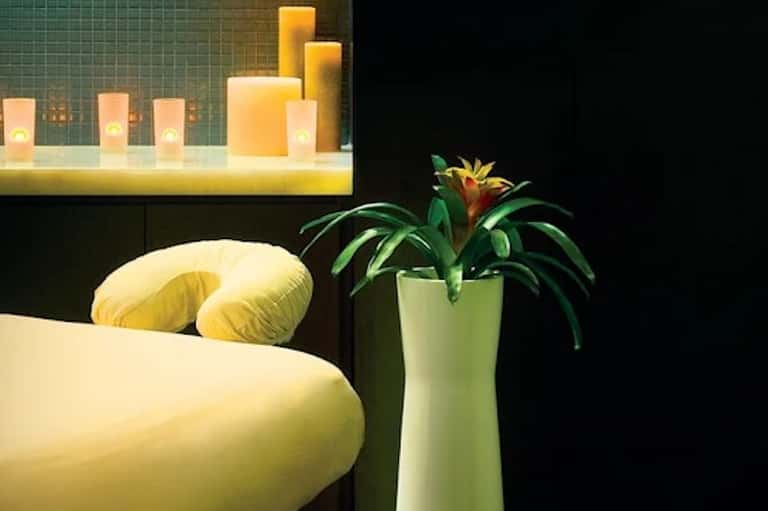 Modern spa bedroom detail with yellow pillows, green tile accent wall, and lit candle shelf