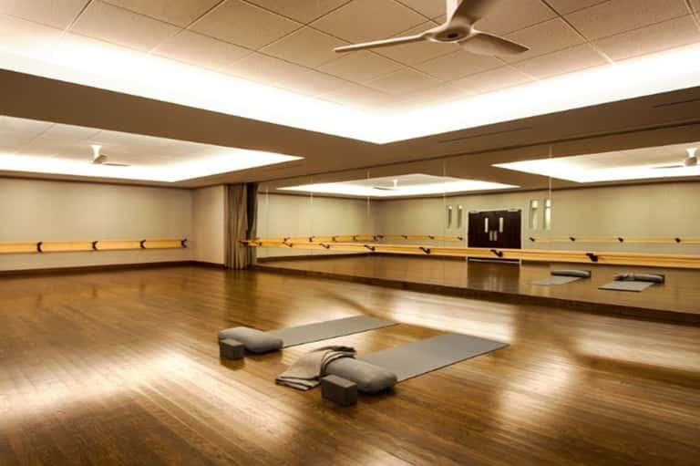 Empty dance studio with wooden floors, mirrored walls, ballet barres, and recessed ceiling lights