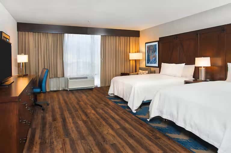 Hotel room with two queen beds, wood furniture, and city view windows