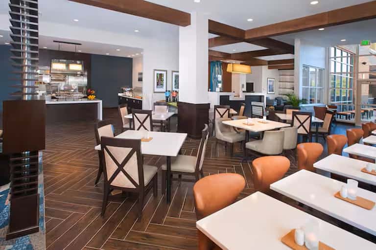 Hotel restaurant dining area with herringbone flooring, booths, tables, and modern kitchen visible