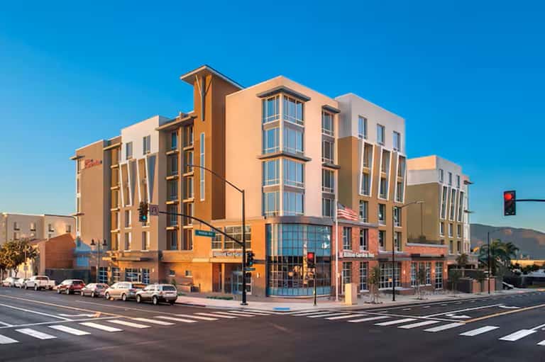 Contemporary mixed-use building with warm orange and beige facade, multiple stories, street-level retail, clear blue sky