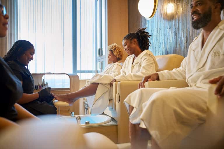 Spa relaxation area with guests in robes, cream seating, modern lighting, and floor-to-ceiling windows