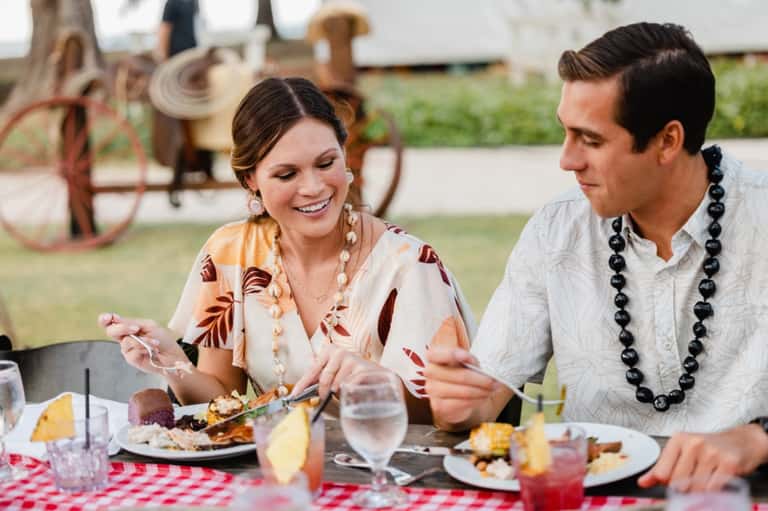 Couple dining outdoors at table with vintage farm equipment visible in background