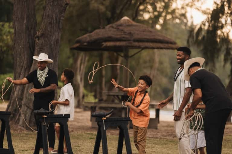 Group of people enjoying rope activities and lawn games under tiki umbrella in grassy resort area