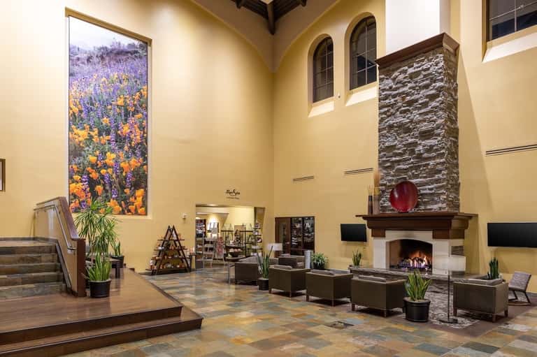 Grand resort lobby with high ceilings, fireplace, stone accents, yellow walls, large floral artwork, and elegant furnishings