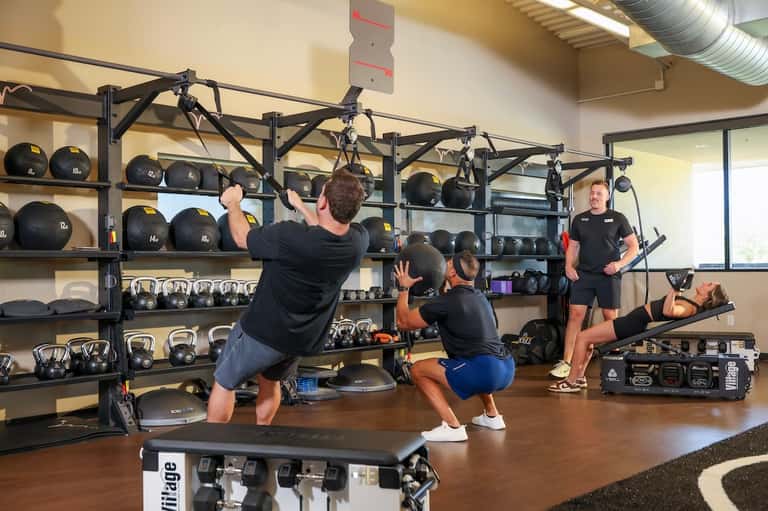 Group fitness class in motion with suspended equipment, medicine balls, and instructor in gym