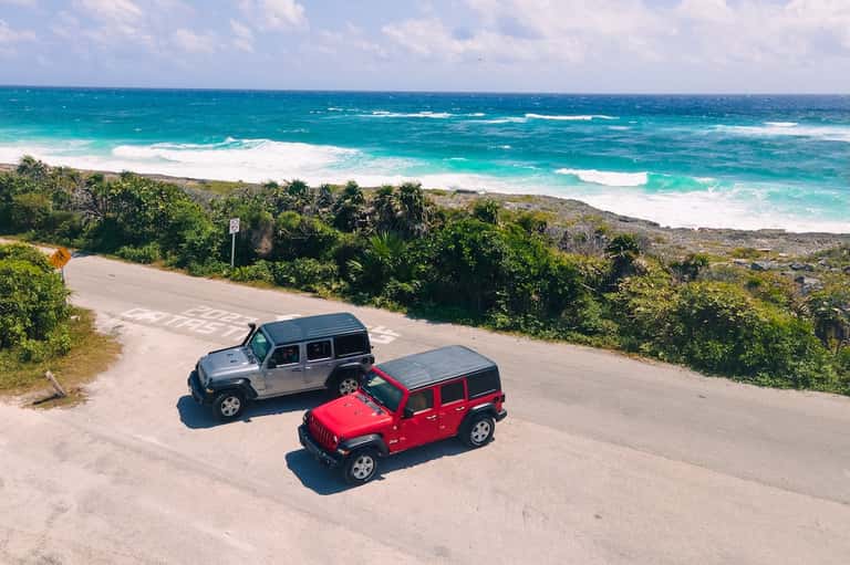 Aerial view of red and gray Jeeps parked on coastal road overlooking turquoise ocean