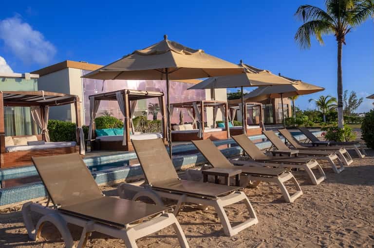 Beach club with cabanas, umbrellas, lounge chairs on sand near water