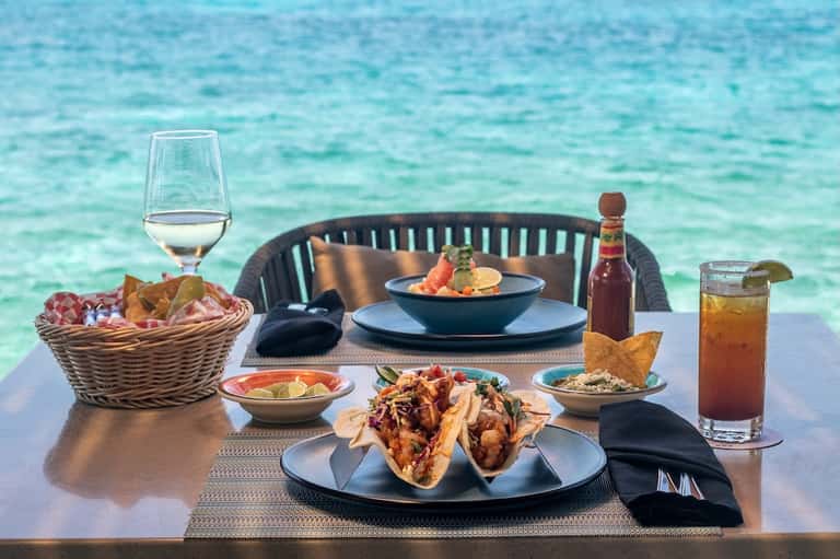 Beachfront dining table with seafood appetizers, cocktails, ocean view, and woven chair
