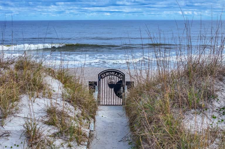 Private beach access gate surrounded by dune grasses and ocean waves in background