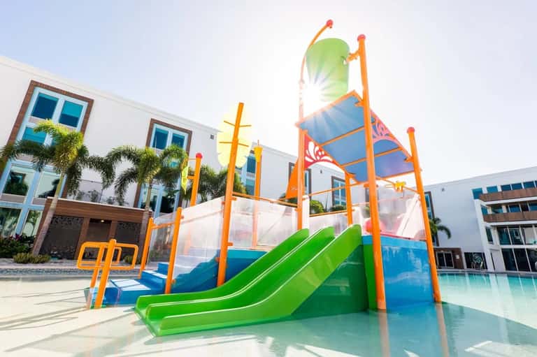 Colorful children's playground with green slide, bright orange frame, and modern residential building