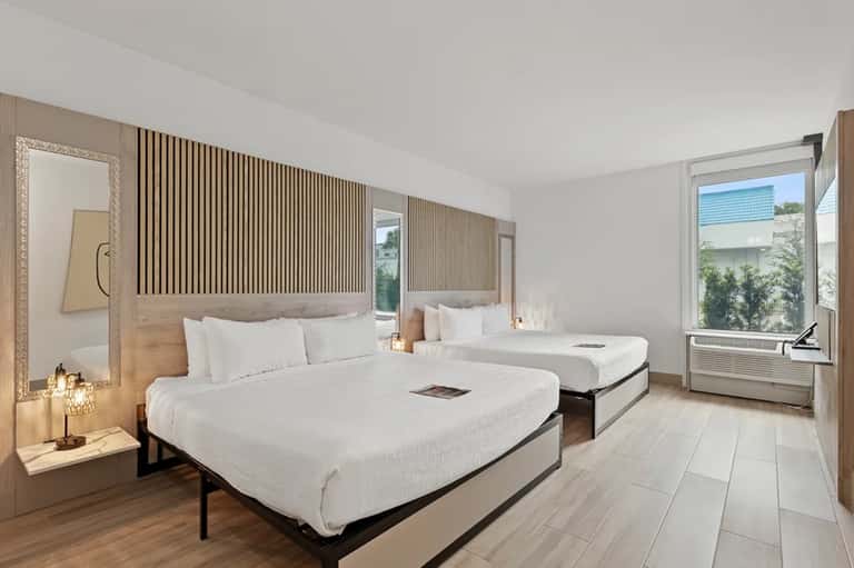 Modern hotel room with two queen beds, wooden accent wall, and contemporary furnishings