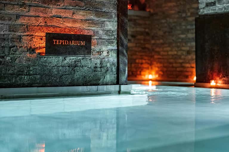 Steaming geothermal pool with Tepidarium sign on weathered brick wall and warm lighting