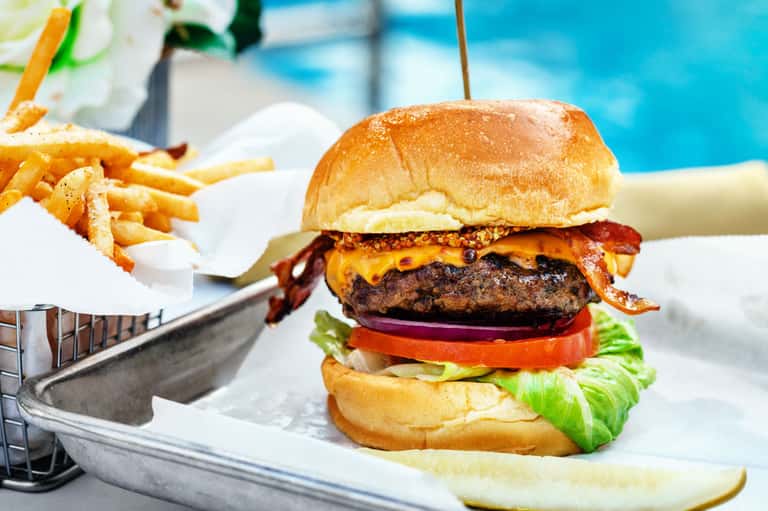 Gourmet burger with fries and lime served poolside with blurred blue water background
