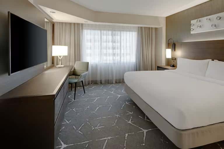 Contemporary hotel room with queen bed, flat-screen TV, desk, and floor-to-ceiling windows