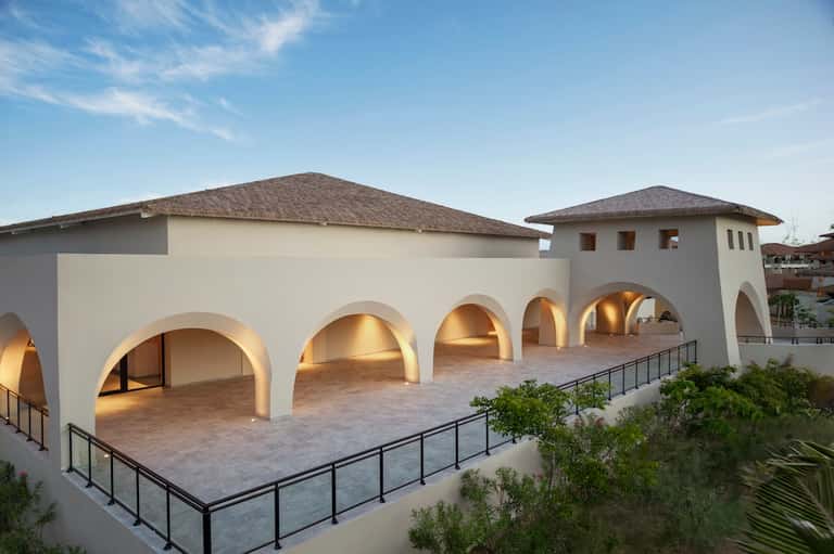 Contemporary white building with arched colonnade, travertine terrace, and dramatic lighting at dusk