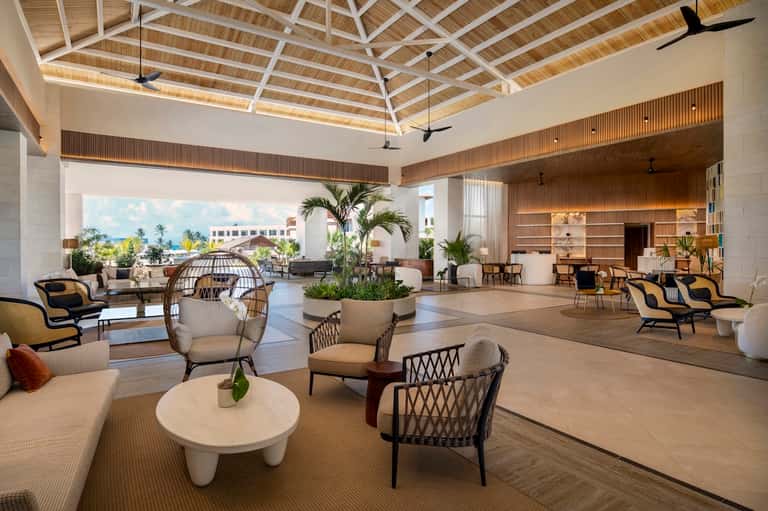 Spacious resort lobby with soaring wood ceiling, tropical plants, modern seating, and ocean views
