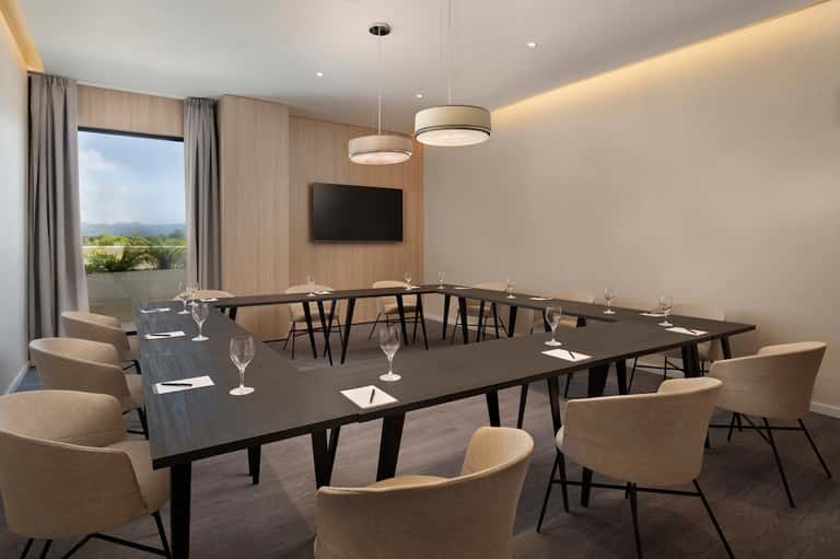 Meeting room with U-shaped table setup, beige chairs, pendant lights, and mountain view