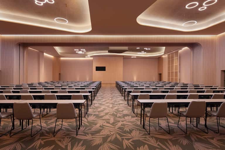Large conference room with theater-style seating, modern ceiling lighting, and neutral décor