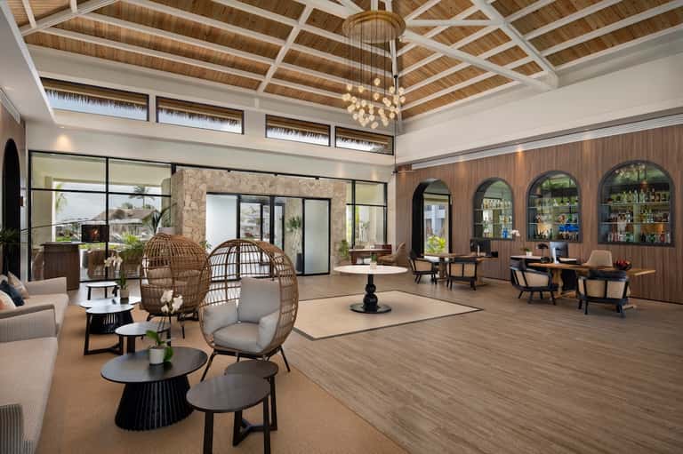 Elegant resort lobby with pendant chandelier, woven chair seating, bar, and high wood-beam ceiling