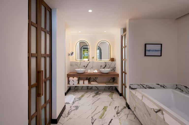 Modern bathroom with dual vessel sinks, marble countertop, arched mirrors, and soaking tub