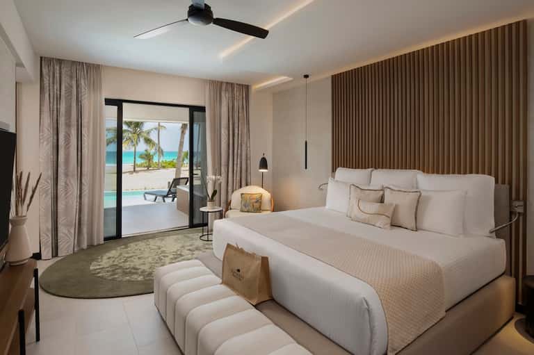 Luxury beach room with king bed, ocean-view patio doors, neutral tones, and modern furnishings