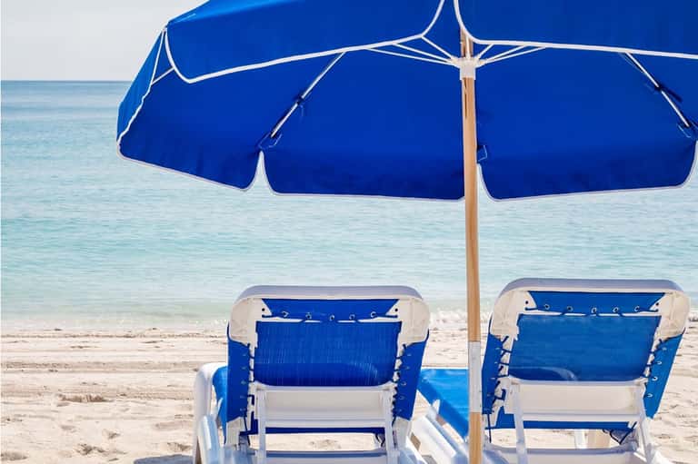 Blue beach umbrella with white lounge chairs overlooking turquoise ocean water