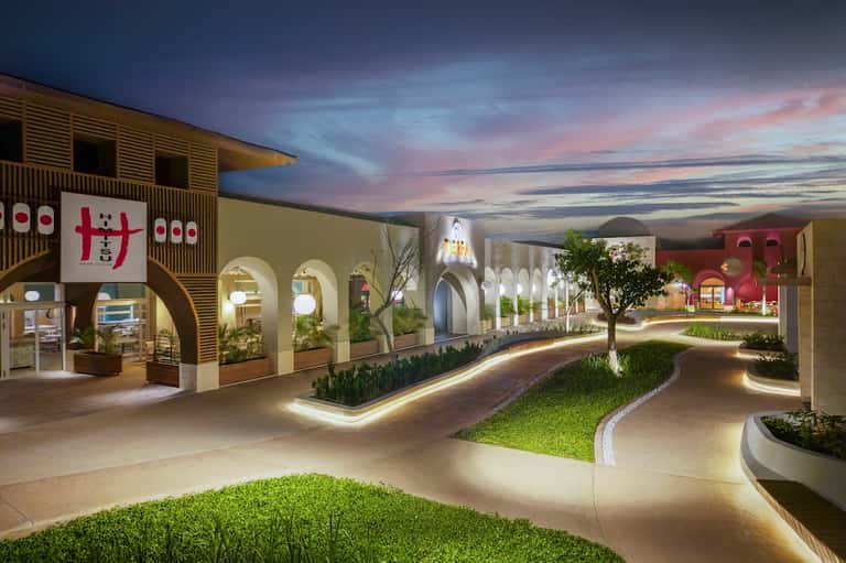 Modern indoor shopping promenade with arched architecture, colorful storefronts, illuminated pathways, and evening sky