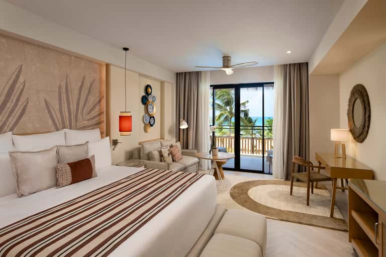 Beachfront hotel bedroom with ocean view, balcony, tropical decor, and modern furnishings
