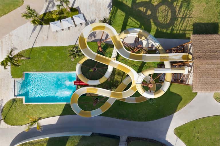 Aerial view of pool with curved white and gold slide on green lawn with palm trees
