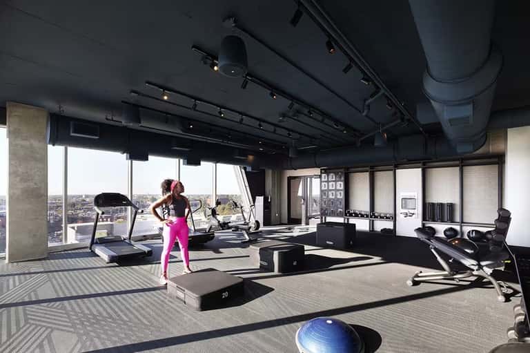 High-rise gym with floor-to-ceiling windows, city views, treadmill, and exercise equipment