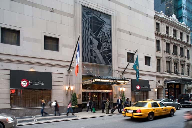 Urban hotel entrance on city street with yellow taxi, flags, and pedestrians