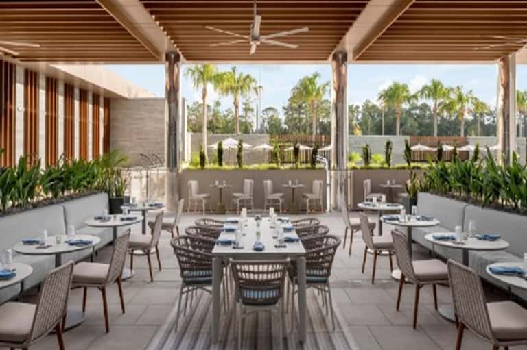 Upscale outdoor dining terrace with pergola, set tables, and palm tree views