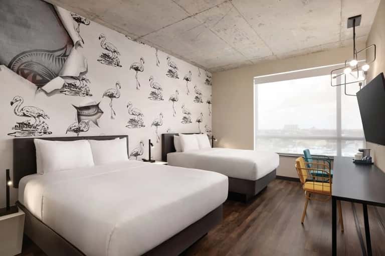 Contemporary hotel room with two beds, flamingo wallpaper, and large window overlooking water