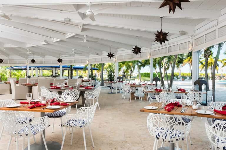 Beachfront dining pavilion with white chairs, wooden tables, decorative stars, and water views