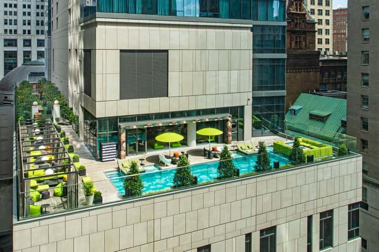 Rooftop pool deck with turquoise water, lime green umbrellas, loungers, and urban cityscape surroundings