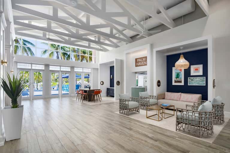 Bright modern lobby with white geometric ceiling, palm trees, blue water views, and contemporary seating area