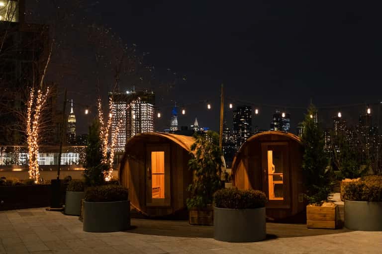 Rooftop wooden sauna pods with city skyline at night and illuminated trees