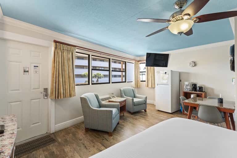 Spacious guest suite with light blue ceiling, comfortable seating, kitchenette, and large windows overlooking water