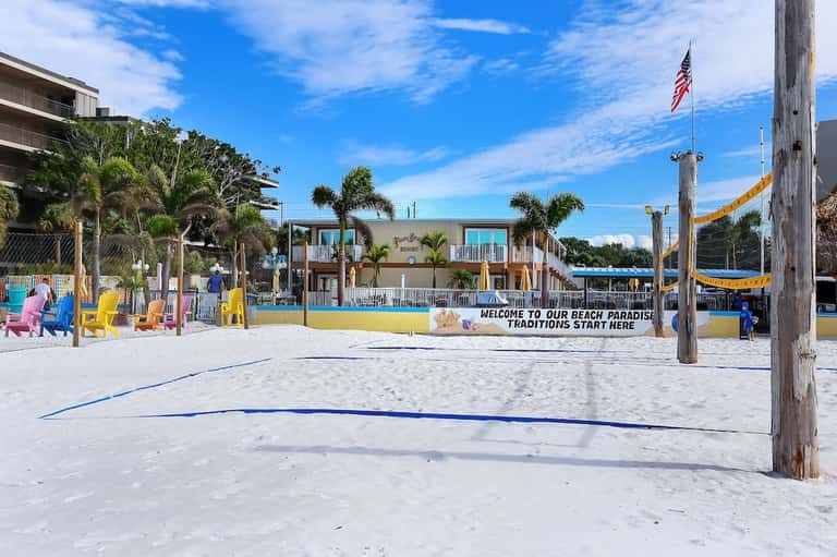 Colorful beachside recreation area with volleyball court, cabanas, and palm trees
