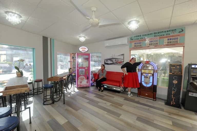 Retro-themed hotel lobby with red sofa, vintage jukebox, vending machines, and bicycle