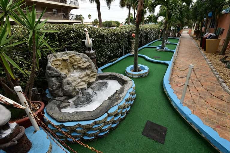 Colorful mini-golf course with tropical landscaping, rock formations, and palm trees