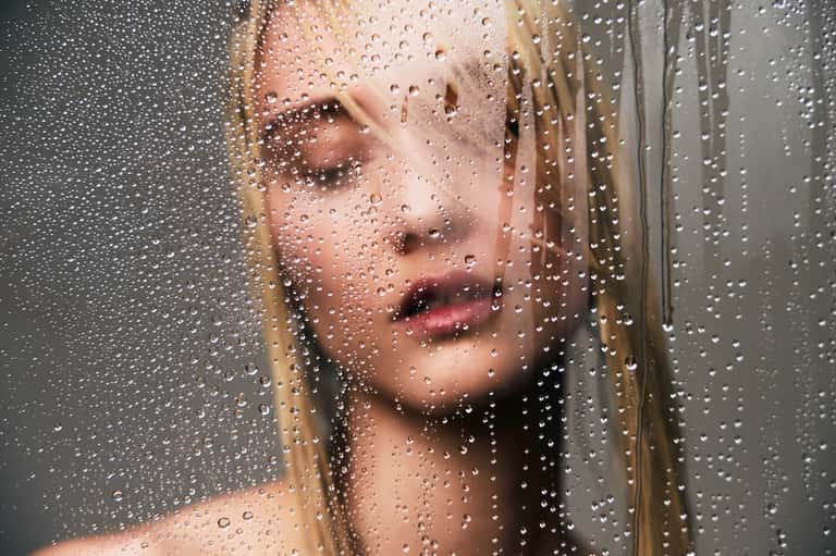 Close-up of woman's face through steamy shower glass with water droplets