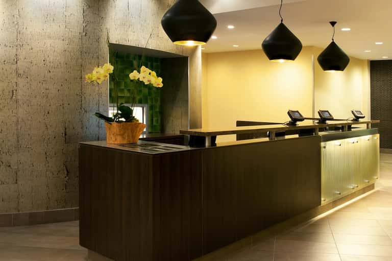 Modern hotel lobby with dark reception desk, yellow orchids, black pendant lights, concrete walls