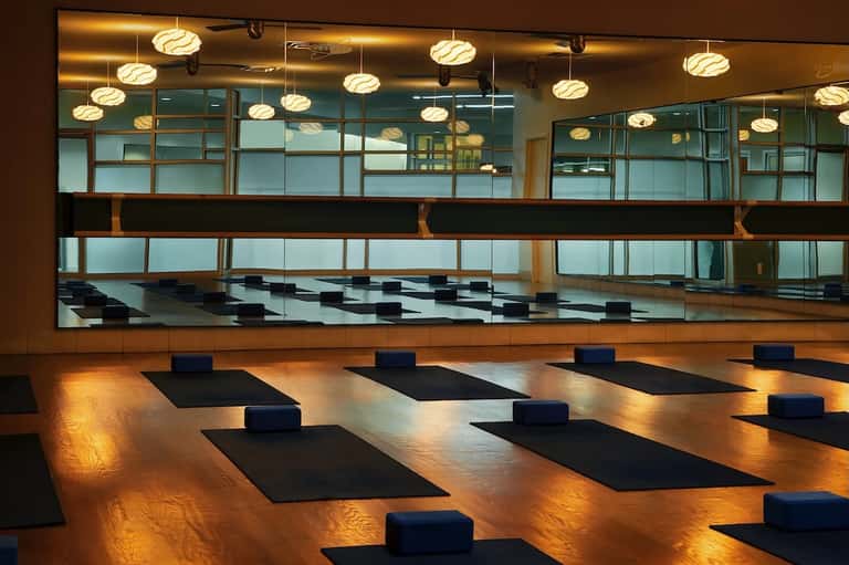 Yoga studio interior with wooden floor, mirrors, pendant lighting, blue bolsters on black yoga mats