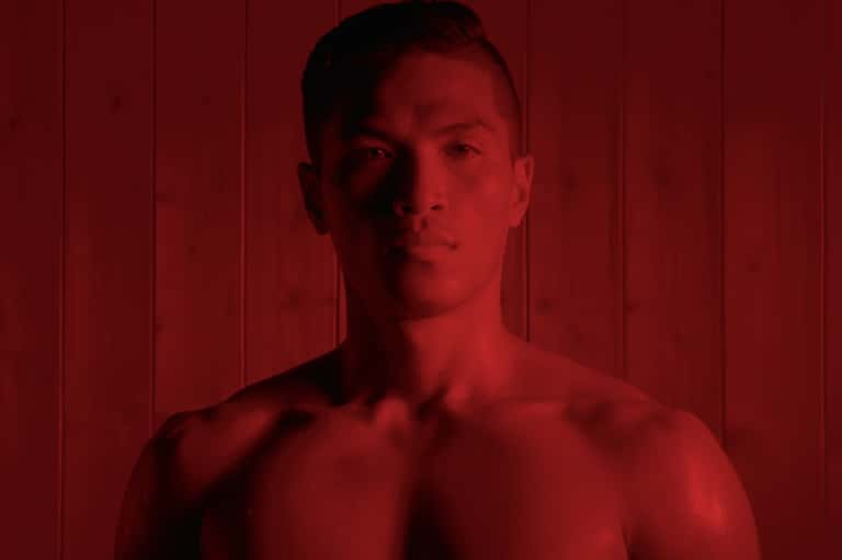 Portrait of shirtless man against red paneled background in moody lighting